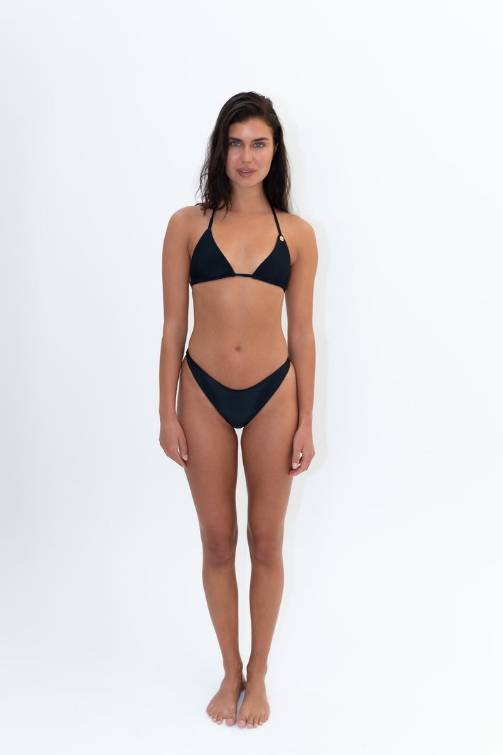 Full-length studio image of a model wearing the MAIU black ribbed bikini bottom paired with the KALLINA black triangle bikini top by Almaya Swimwear.